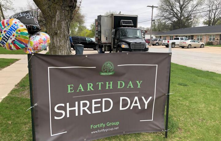 A gray and green Shred Day for Earth Day banner is shown in the foreground. The Paper Tiger mobile shredding truck sits in the background.