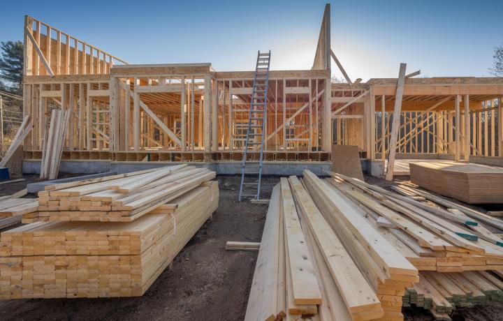 The frame of a new home is taking shape in this construction site photo. In the foreground, piles of lumber are stacked, ready for use. waiting to be used 