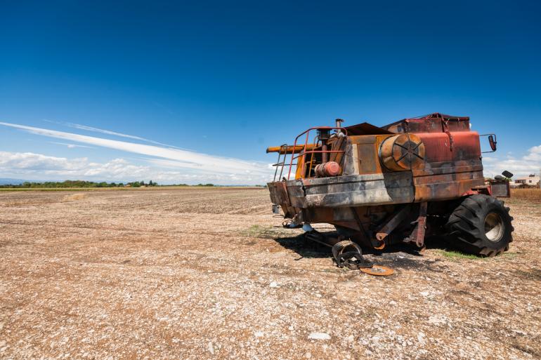 A burned, unusable red combine remains in a barren field following a combine fire. The sky above is a vivid blue.