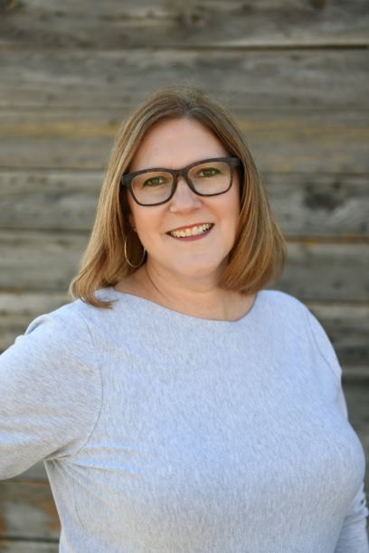 Realtor Kate Manes is pictured in this professional portrait. She is wearing stylish glasses with a light gray sweater.