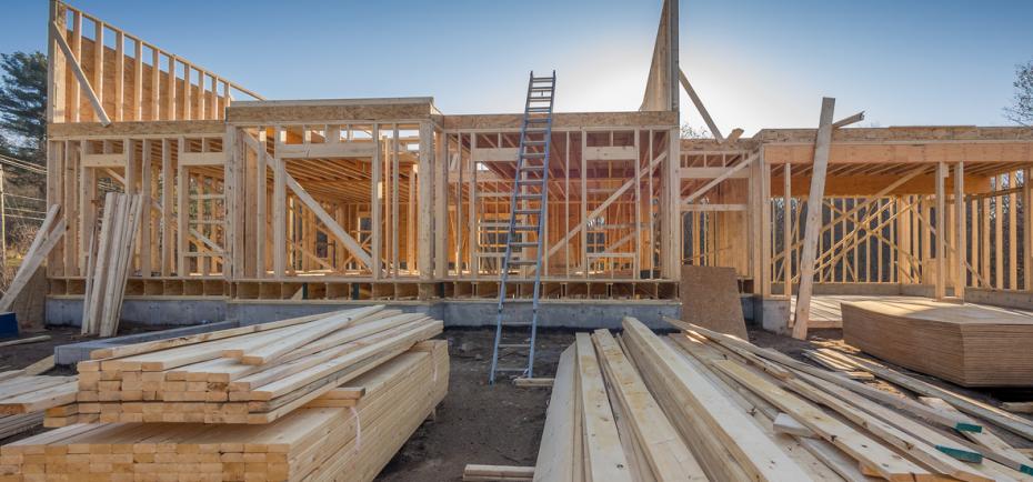 The frame of a new home is taking shape in this construction site photo. In the foreground, piles of lumber are stacked, ready for use. waiting to be used