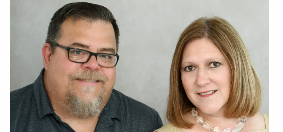 New Fortify Group team members Jim and Kate Manes are pictured in this professional portrait. Jim wears glasses and a gray polo; Kate has on a pale cream sweater.