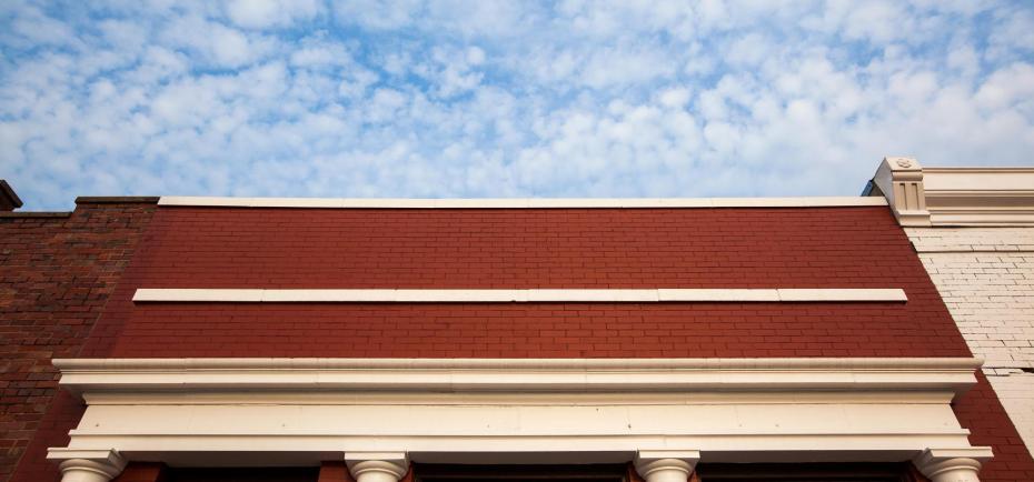 The red brick of the shickley office is pictured against a fluffy blue sky. The photographer shot this photo looking almost straight up at the sky, to highlight the brick and front columns.