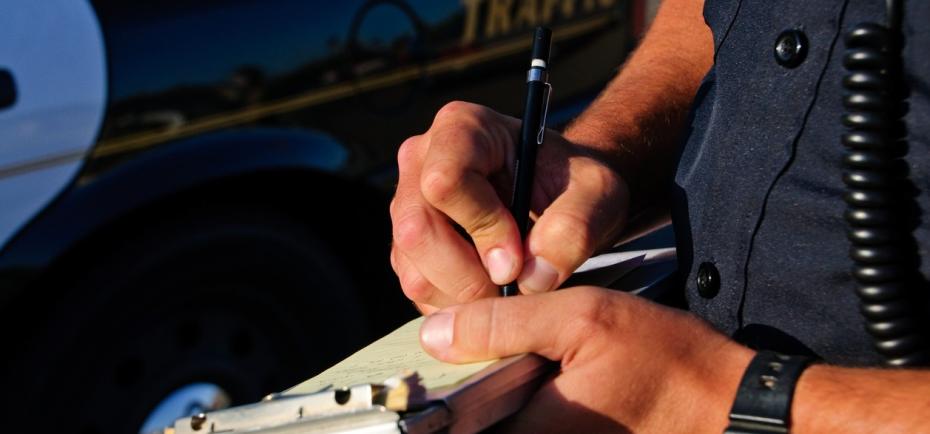 This is a close shot of a law enforcement officer's hands and he writes a citation.
