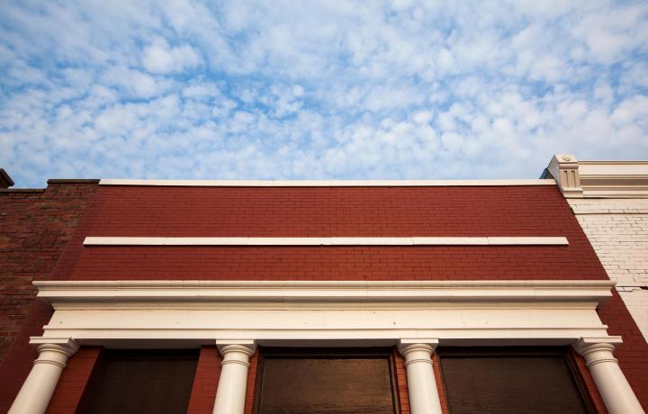 The red brick of the shickley office is pictured against a fluffy blue sky. The photographer shot this photo looking almost straight up at the sky, to highlight the brick and front columns.
