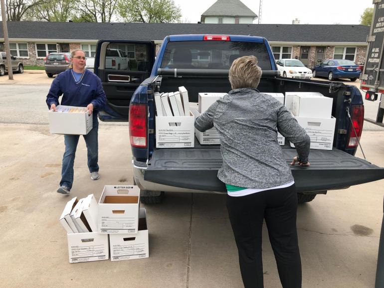 A Fortify Group customer carries a box of old files and documents to the curb, while a Fortify employee helps unload a pickup bed full of more white boxes.