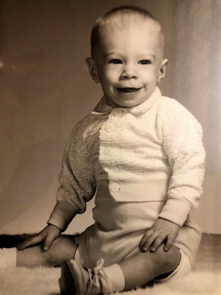 Bart Brinkman is pictured at about 9 months of age. He is wearing a white baby sweater, shorts and shoes.