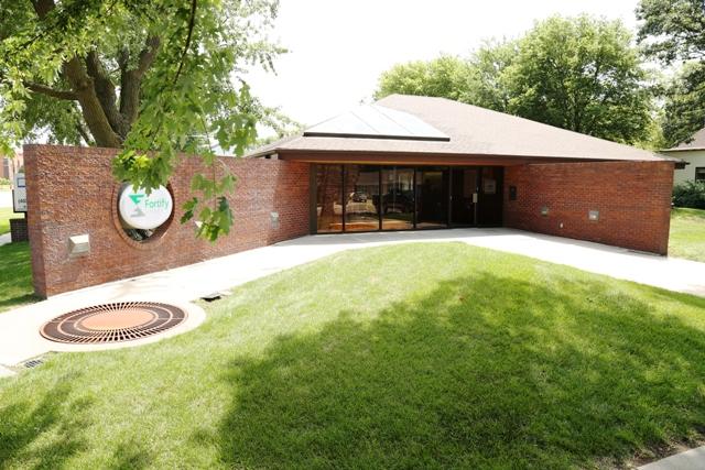 The Geneva office is pictured on a sunny day. It is a low-slung brick building with a green space in front.