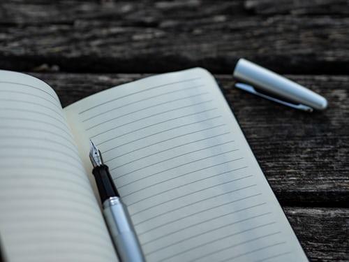 A lined notebook and pen are pictured on a wooden table.