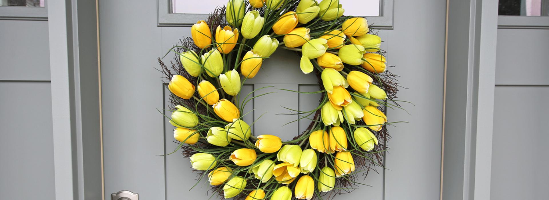 A wreath of striking yellow tulips graces a gray, farmhouse-style front door.