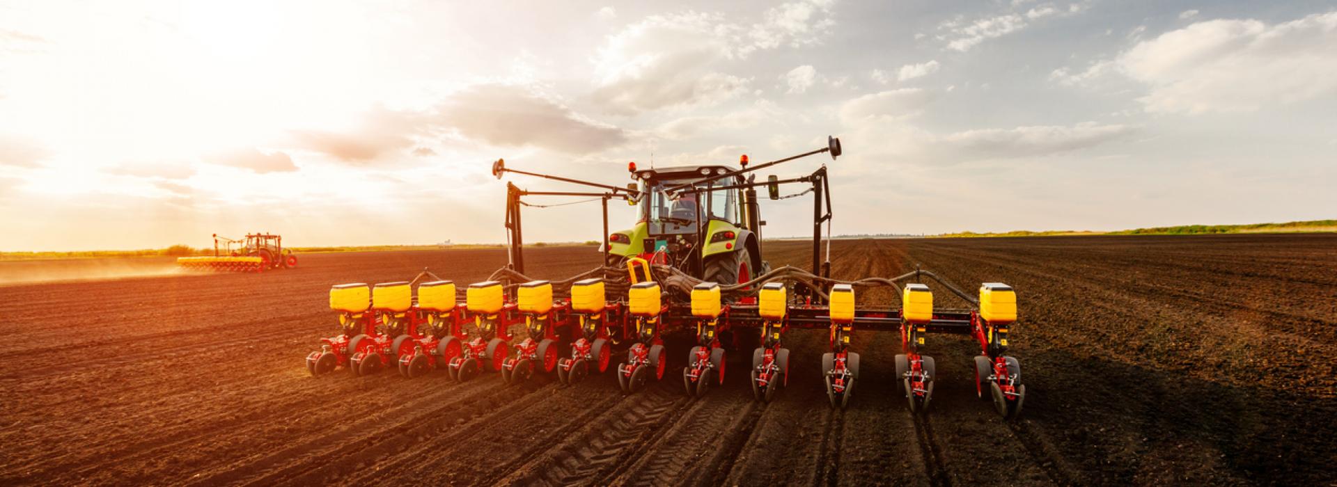 A tractor and planter are pictured planting spring crops at sunset.