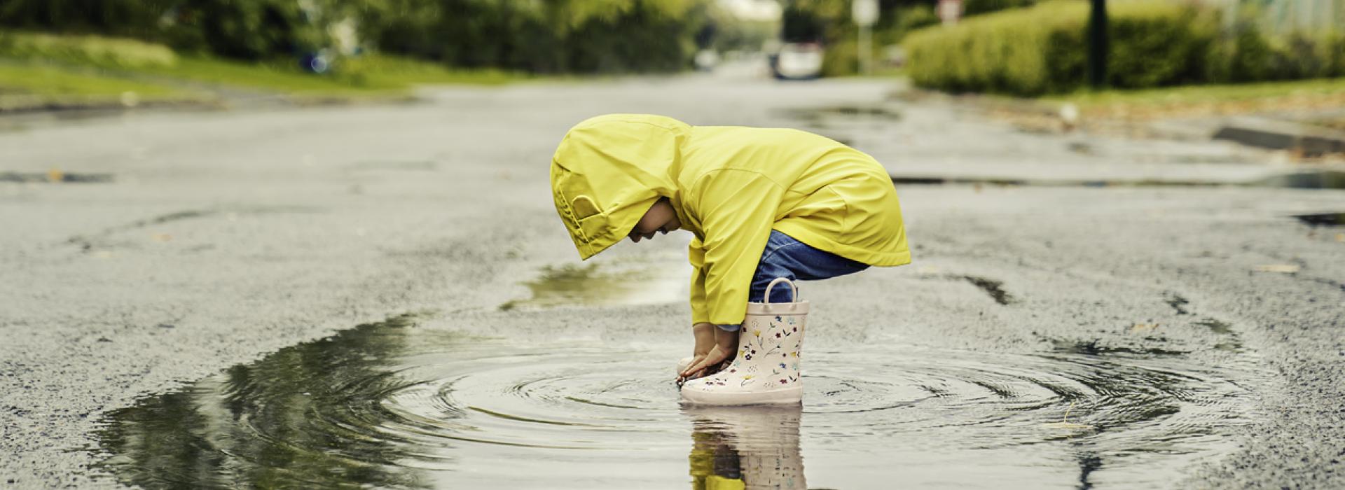 A toddler plays in a rain puddle in a bright yellow rainjacket