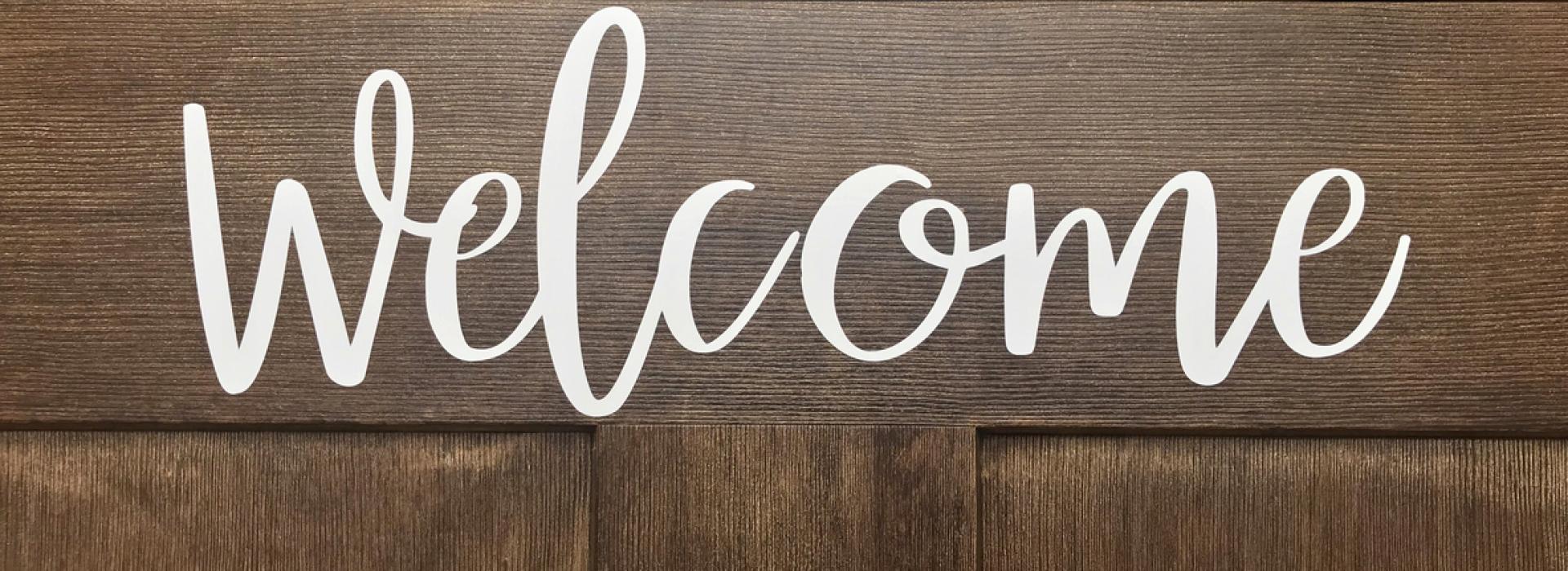 The word "Welcome' is spelled out in a white, cursive stencil on the front of a dark, Craftsmen-style entry door.